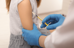 Close up of a syringe going into a young girl's arm, administered by a female with gloves
